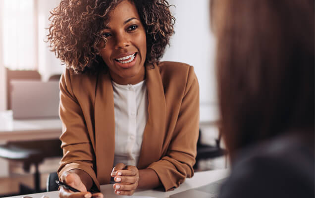Smiling Black woman sitting at desk talking with another woman