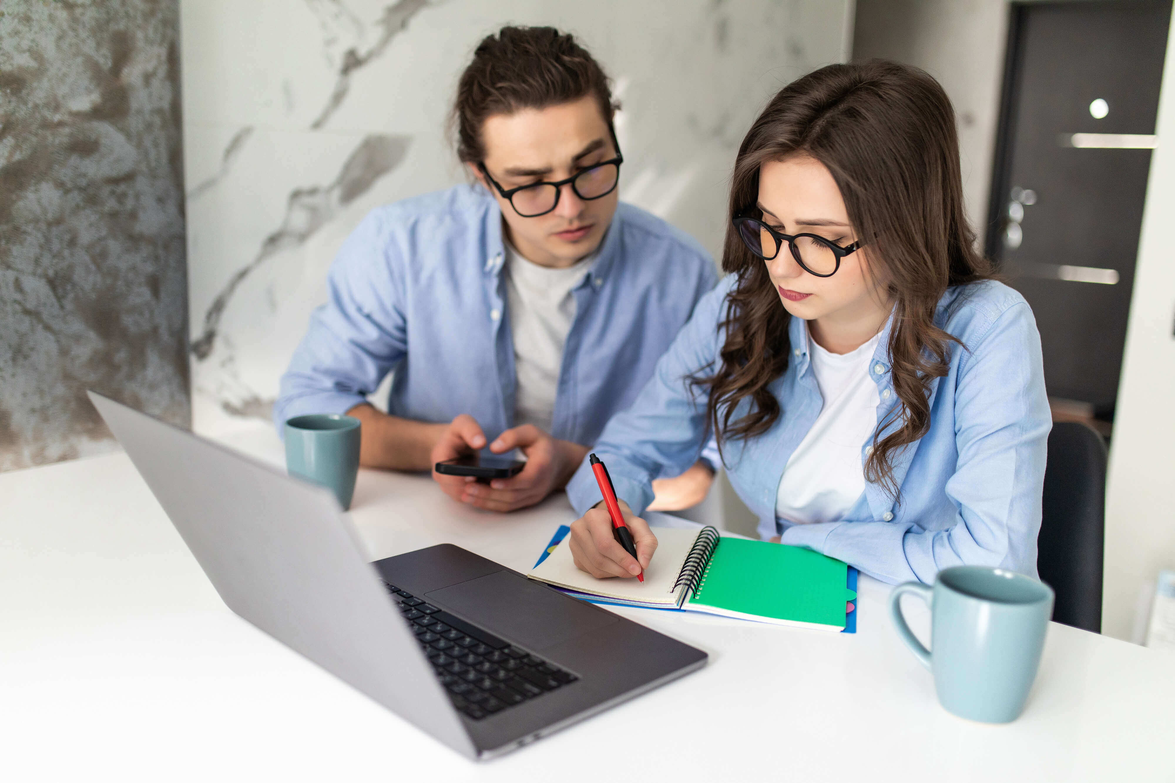 Young couple with laptop and calculator, making notes in notebook